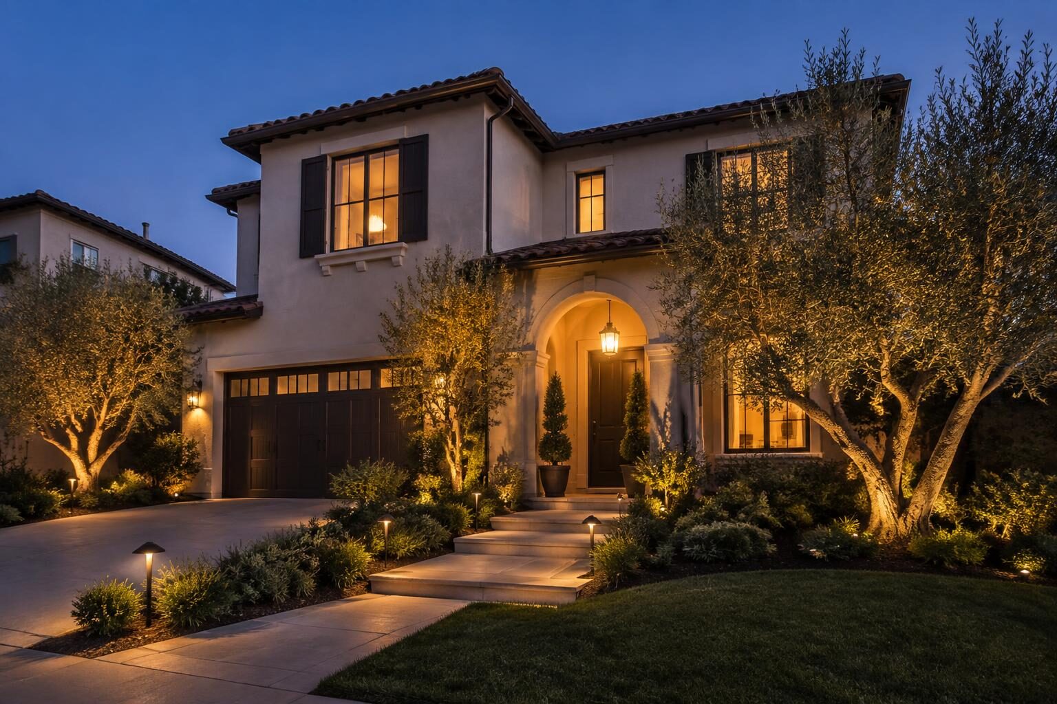 Two-story Los Angeles home with warm landscape lighting on olive trees and the front walkway